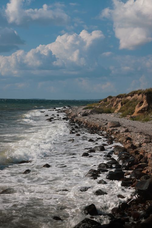 Free Explore the wild beauty of Ebberup's rocky coastline with waves and dramatic clouds. Stock Photo