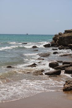 Rocky beach with waves crashing under a clear blue sky.