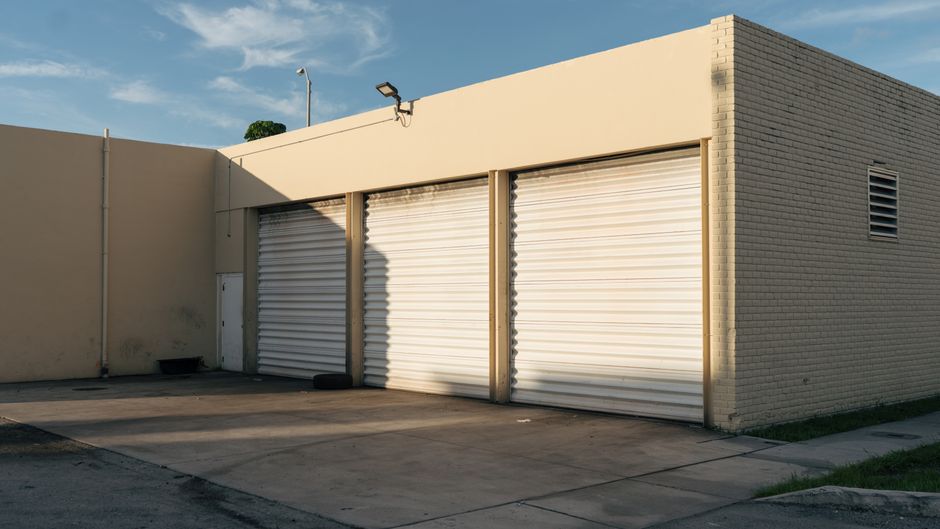 Top Smart Garage Door Openers for 2025: Ultimate Step-by-Step Setup Guide Exterior view of a beige industrial building with three closed garage doors under a clear sky.