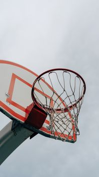A basketball hoop and net set against a backdrop of a cloudy sky, viewed from below.