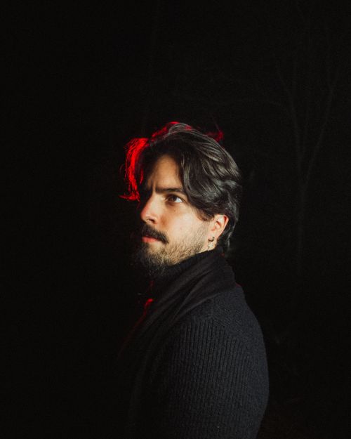 Free A pensive man looks into the distance with dramatic lighting highlighting his profile against a dark background. Stock Photo