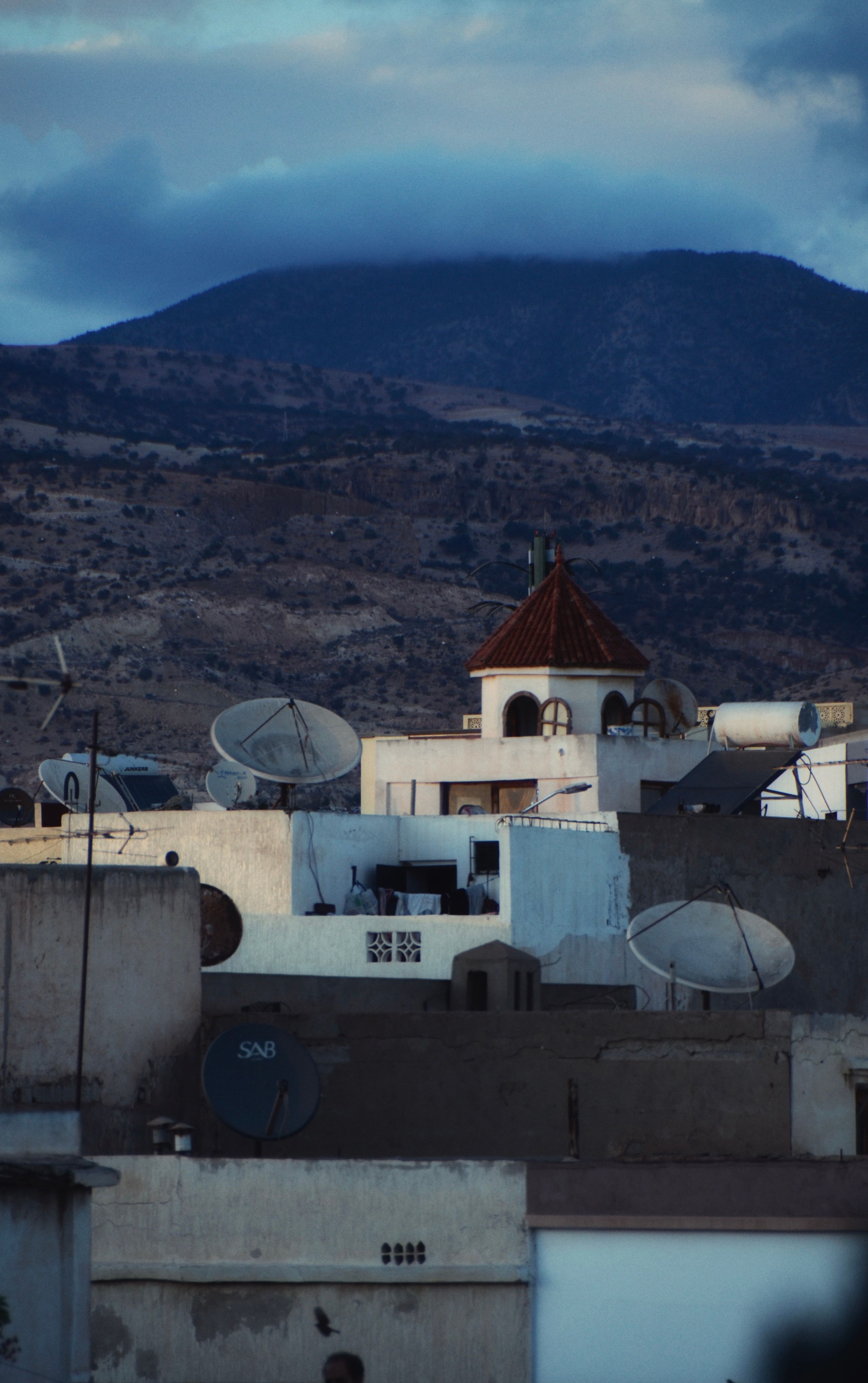 Rustic rooftops and satellite dishes in a Moroccan village at twilight.