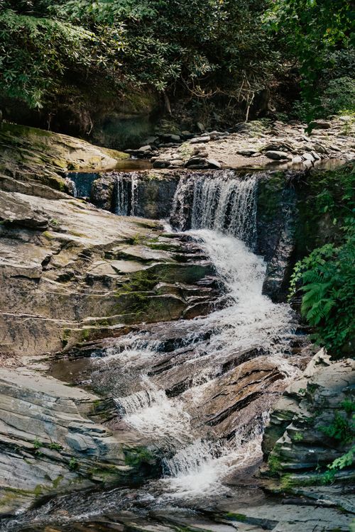 Free Peaceful waterfall flowing over rocks in a lush forest setting. Ideal for nature enthusiasts. Stock Photo