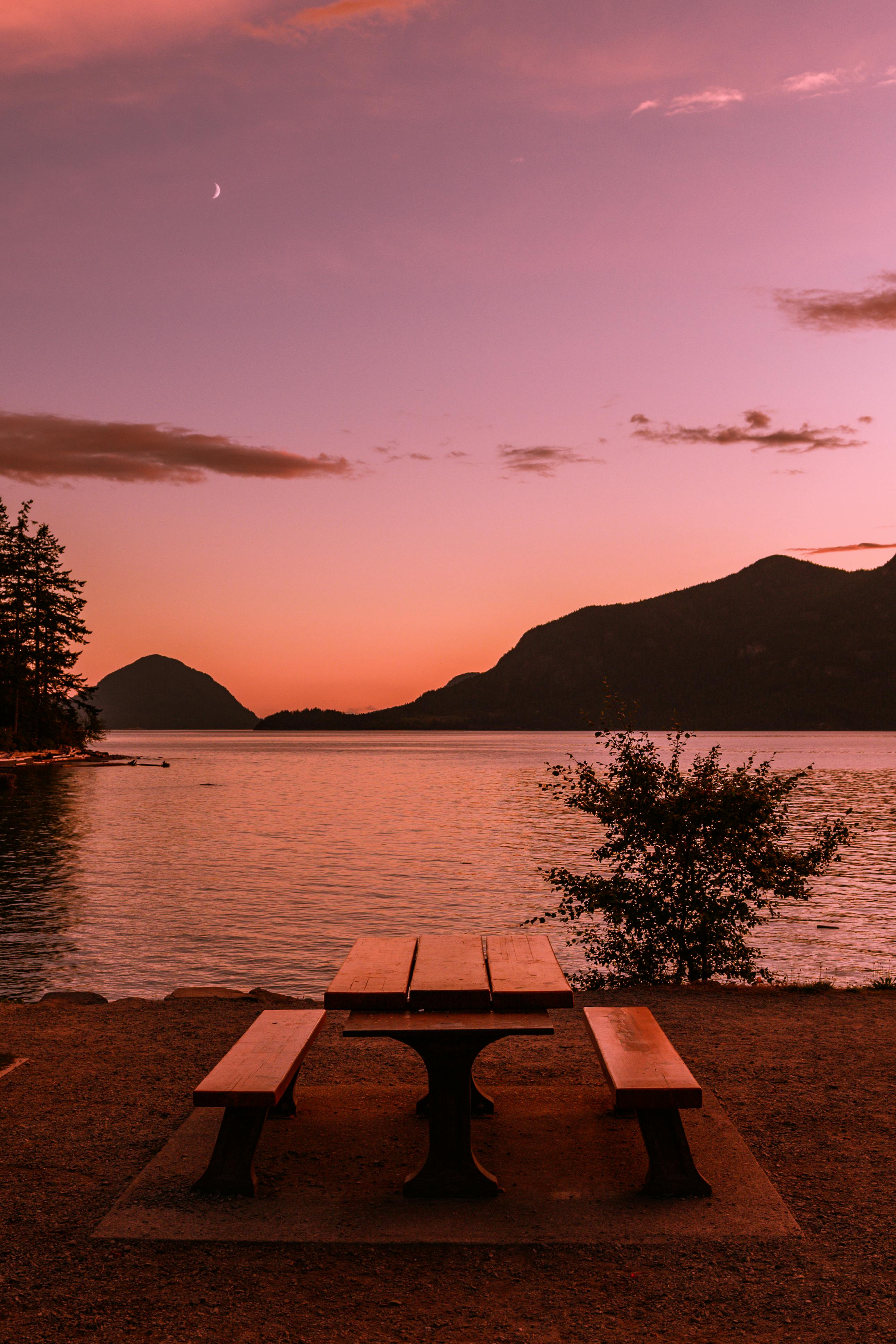 brown wooden table and bench near body of water during sunset