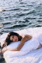 女人躺在白色的床垫上，漂浮在平静的海水之上，体现了宁静和放松