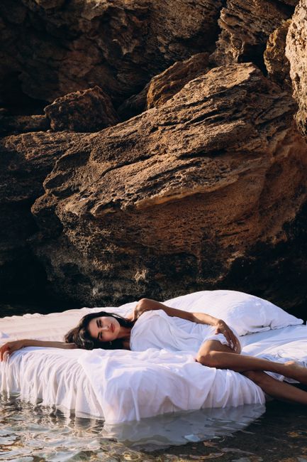 A woman relaxes on a floating bed near rock formations on a sunny day, outdoors.