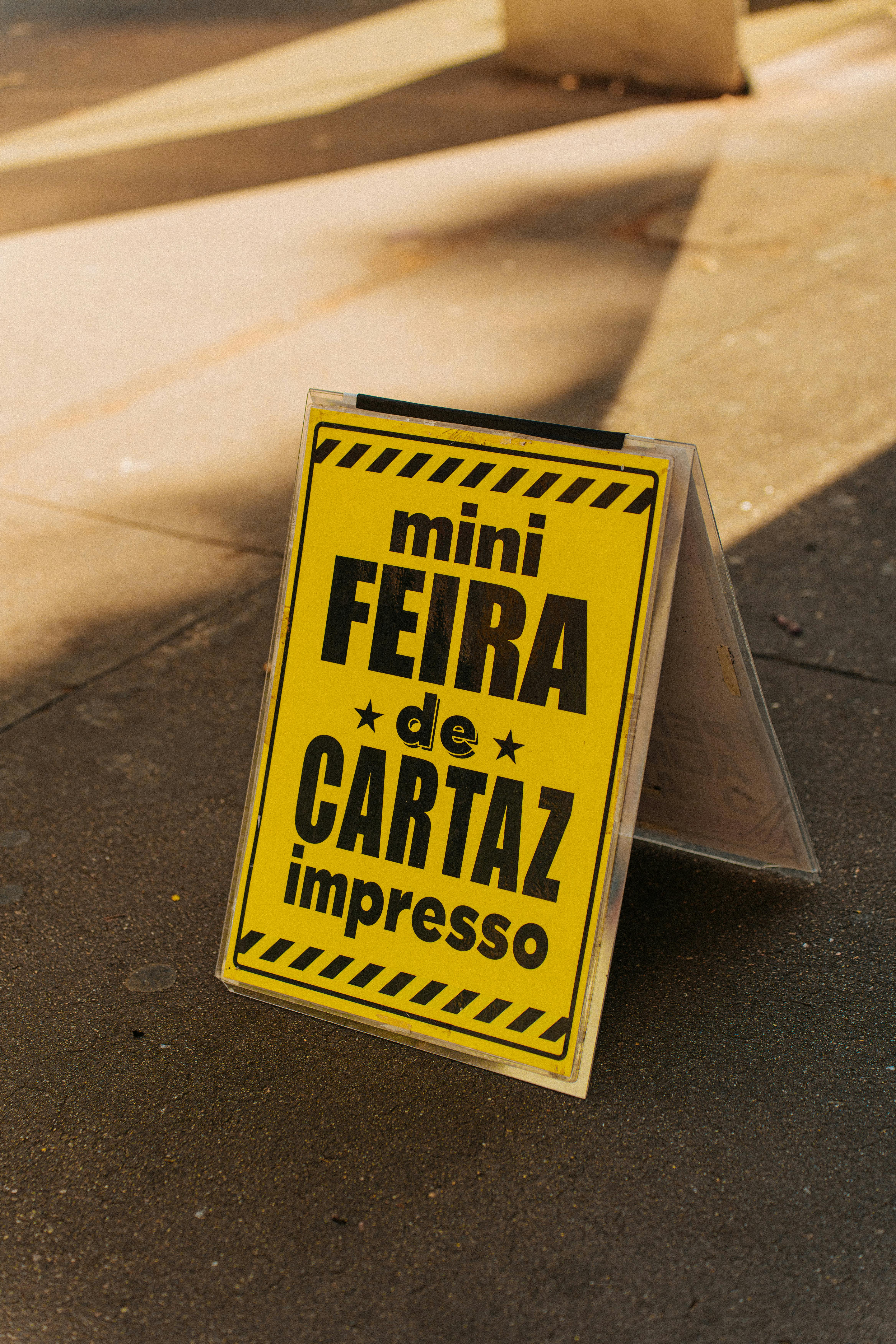 A yellow poster promoting a mini fair event on a sunlit sidewalk in São Paulo, Brazil.