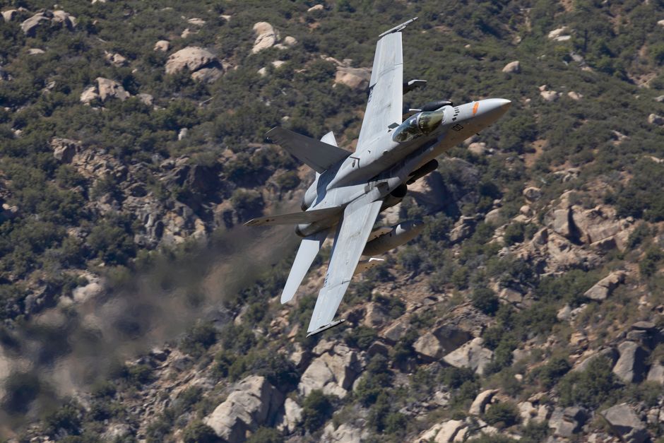 F/A-18 Hornet voert een manoeuvre uit boven het ruige landschap van Californië bij heldere hemel.