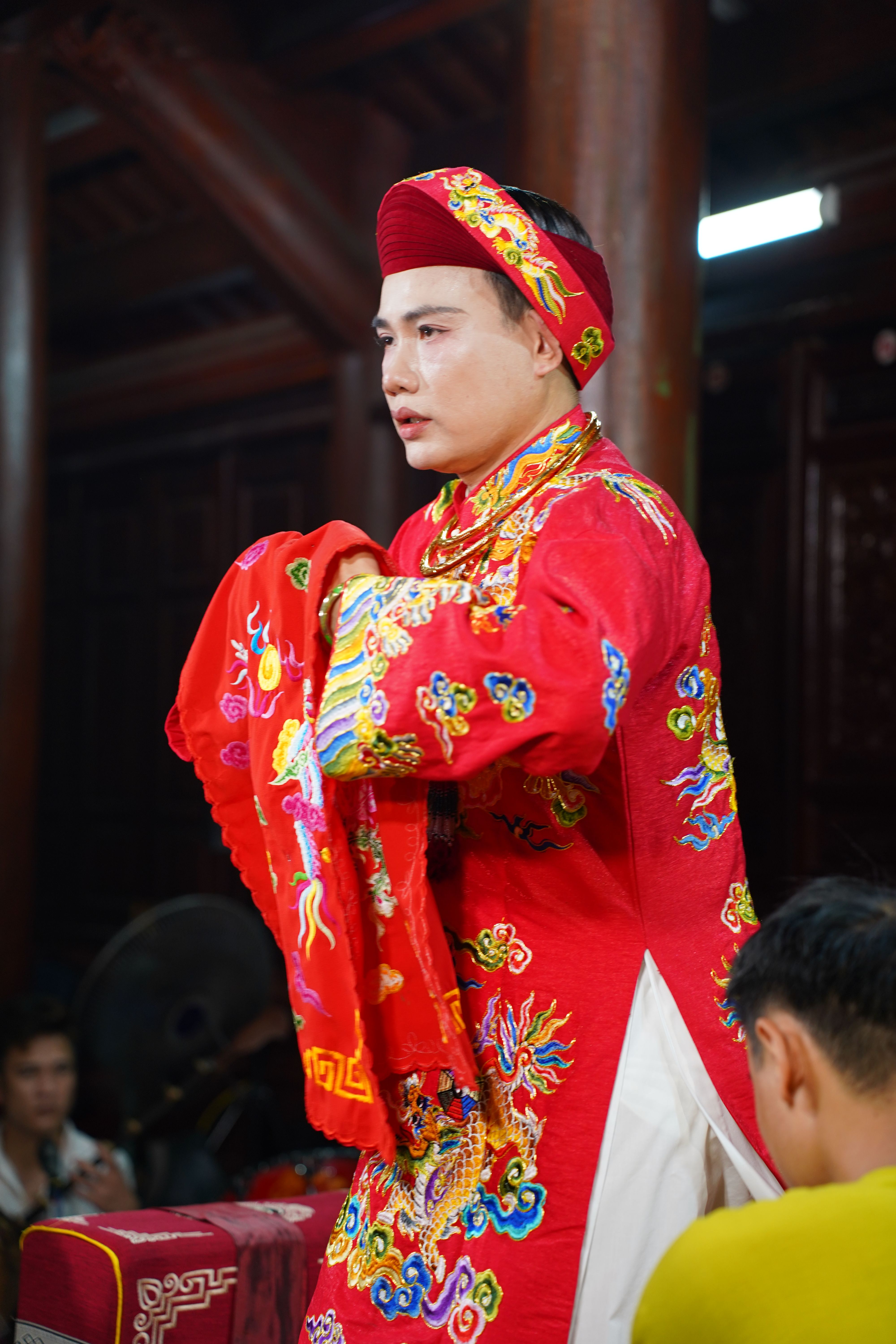 Man in traditional vibrant red attire participates in cultural ceremony indoors.