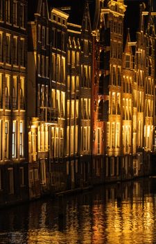 Nighttime view of glowing canal houses reflecting in water in Amsterdam, Netherlands.