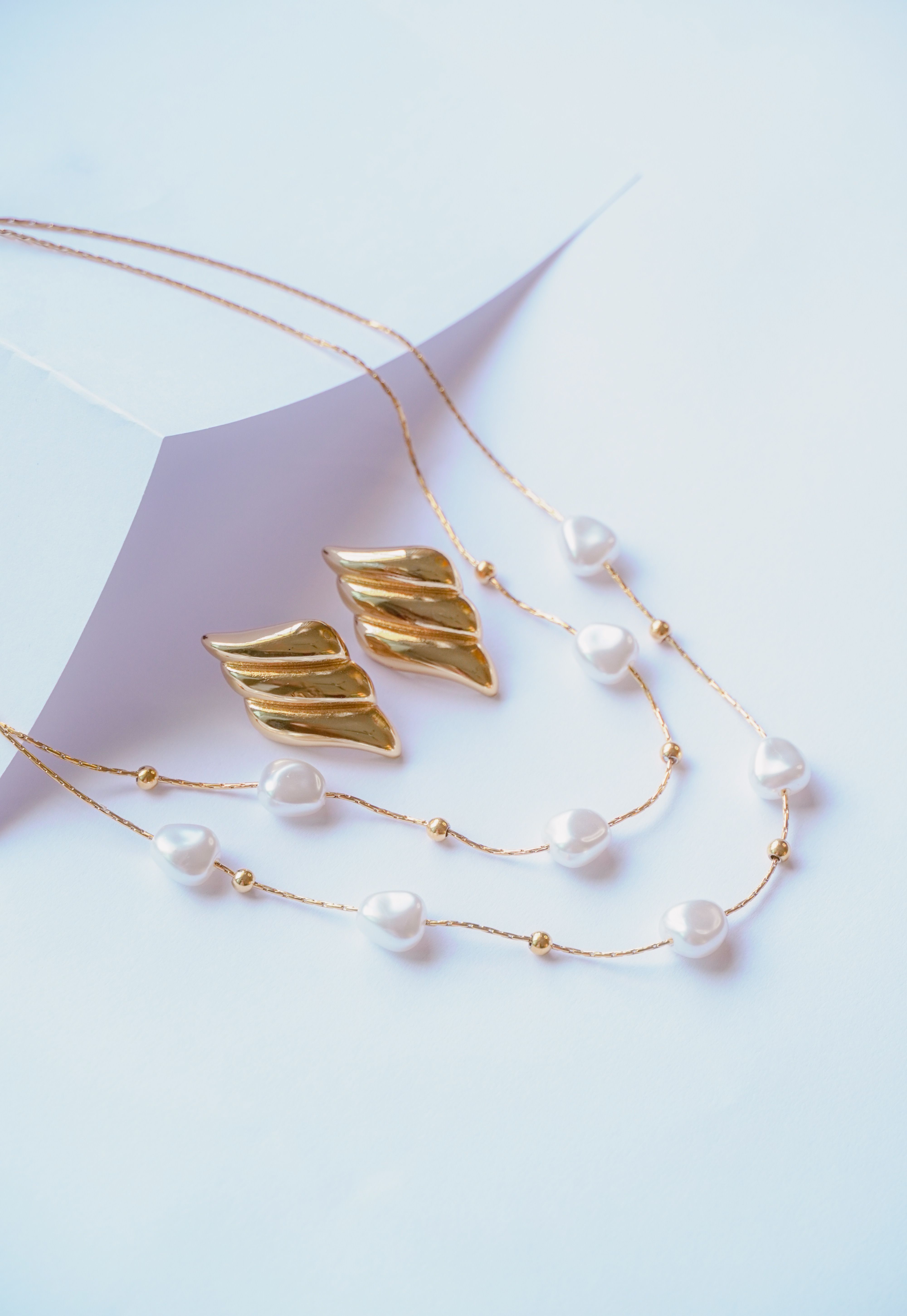Collar de perlas y aretes dorados sobre fondo claro minimalista.