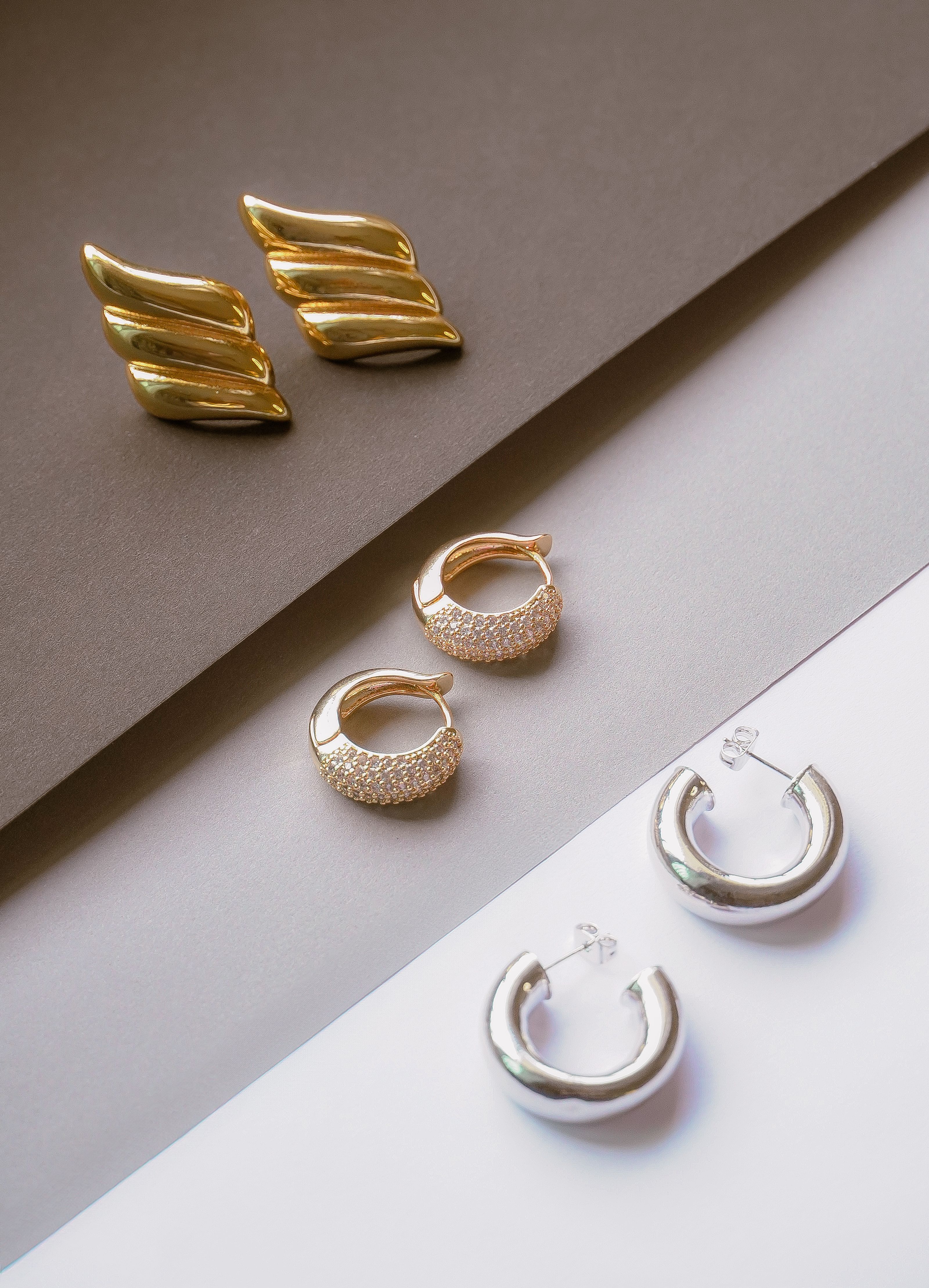 Conjunto chique de brincos de ouro e prata em fundos contrastantes, apresentando um design moderno de joias.