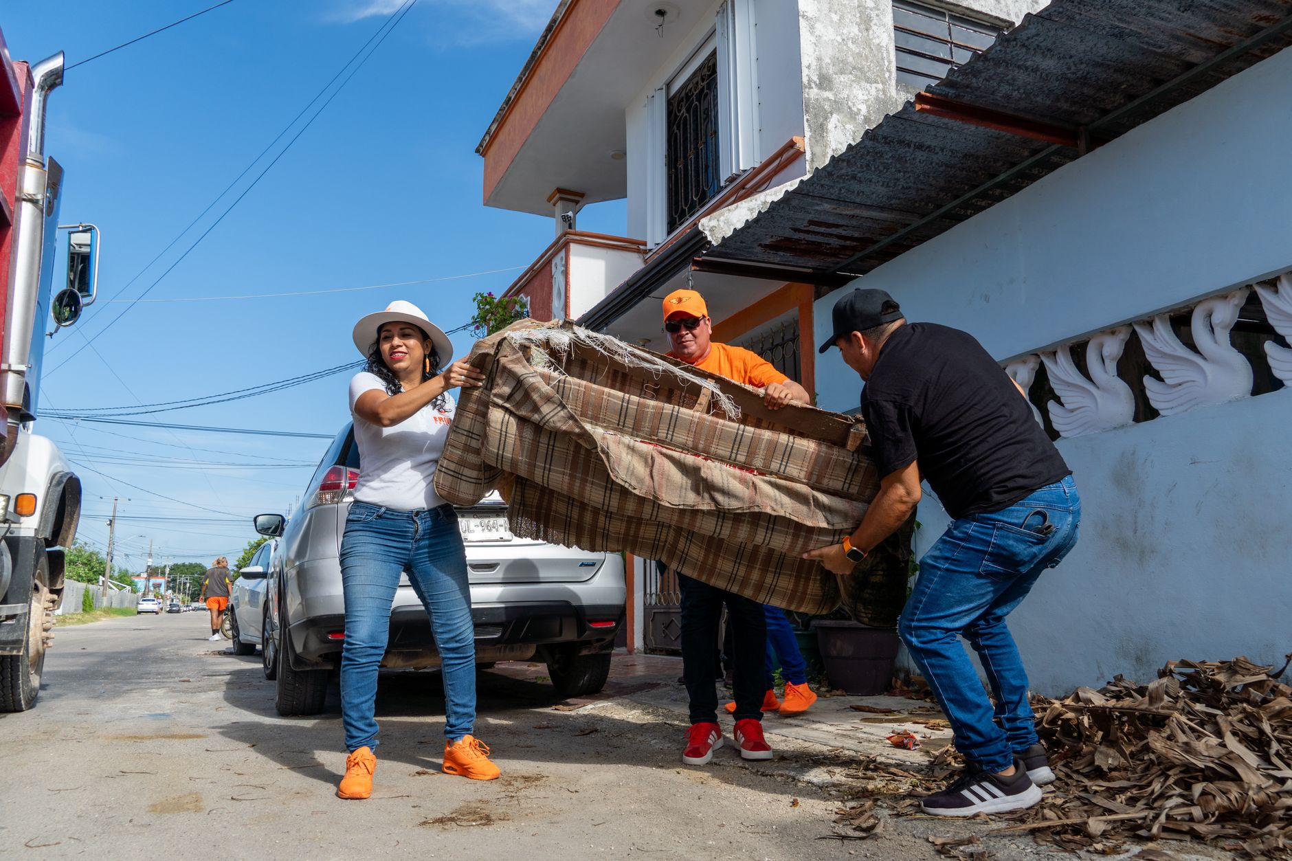 People working together to lift and dispose of furniture outdoors on a sunny day.