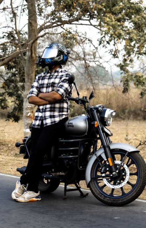 Free Casual man in plaid shirt and helmet leans on Royal Enfield bike on a rural road. Stock Photo