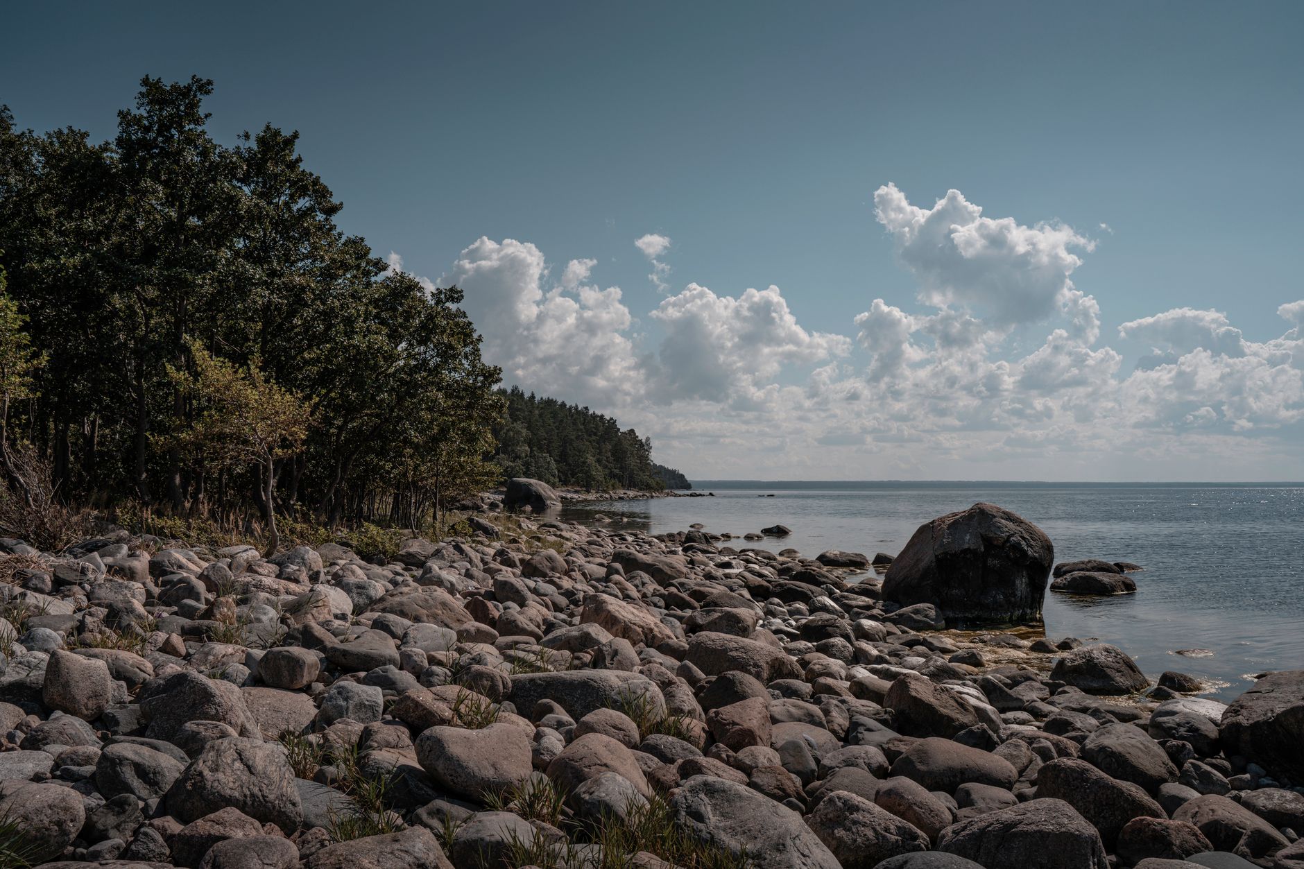 Scenic view of Käsmu's rocky shoreline and serene sea under a blue sky with clouds.