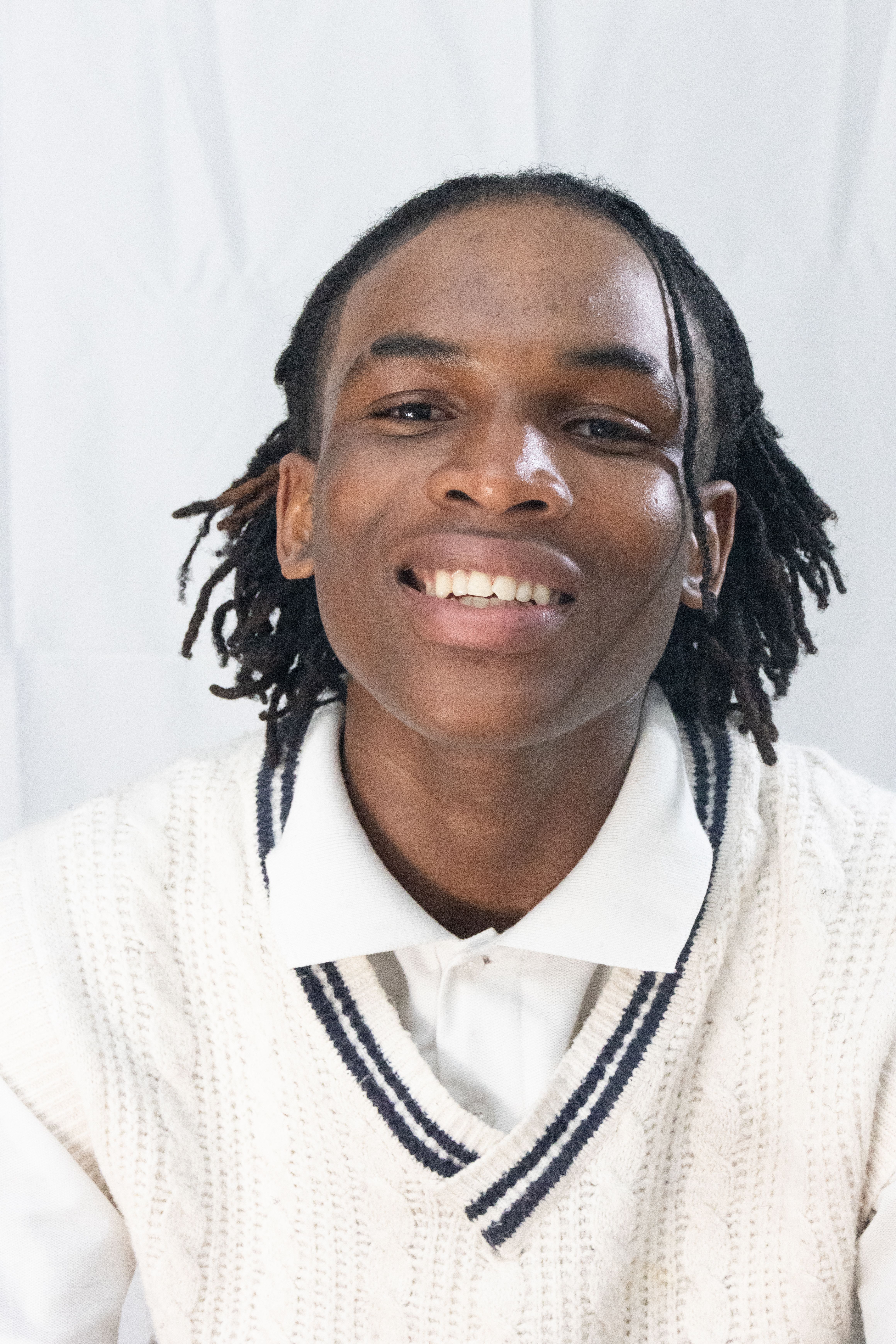 Cheerful young adult wearing a white sweater and shirt, smiling in a portrait shot.