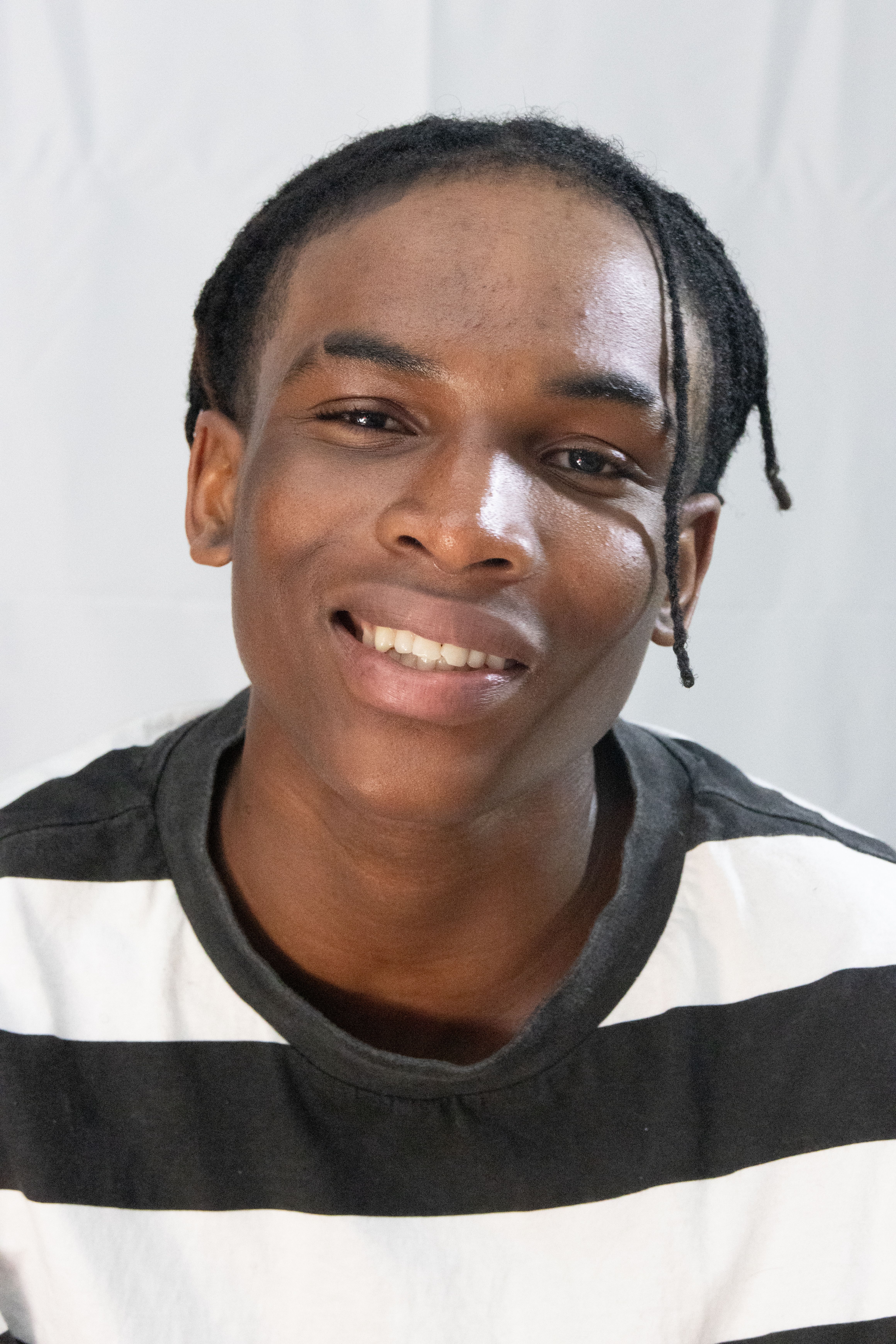 A close-up portrait of a smiling adult wearing a black and white striped shirt, shot indoors.