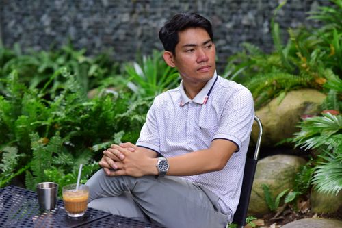 Free A man in casual attire sitting outdoors in a garden, enjoying a beverage. Stock Photo