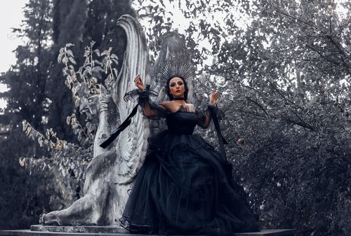 Free A dramatic portrait of a woman in a black gown with a regal and cinematic style set against a stone sculpture. Stock Photo