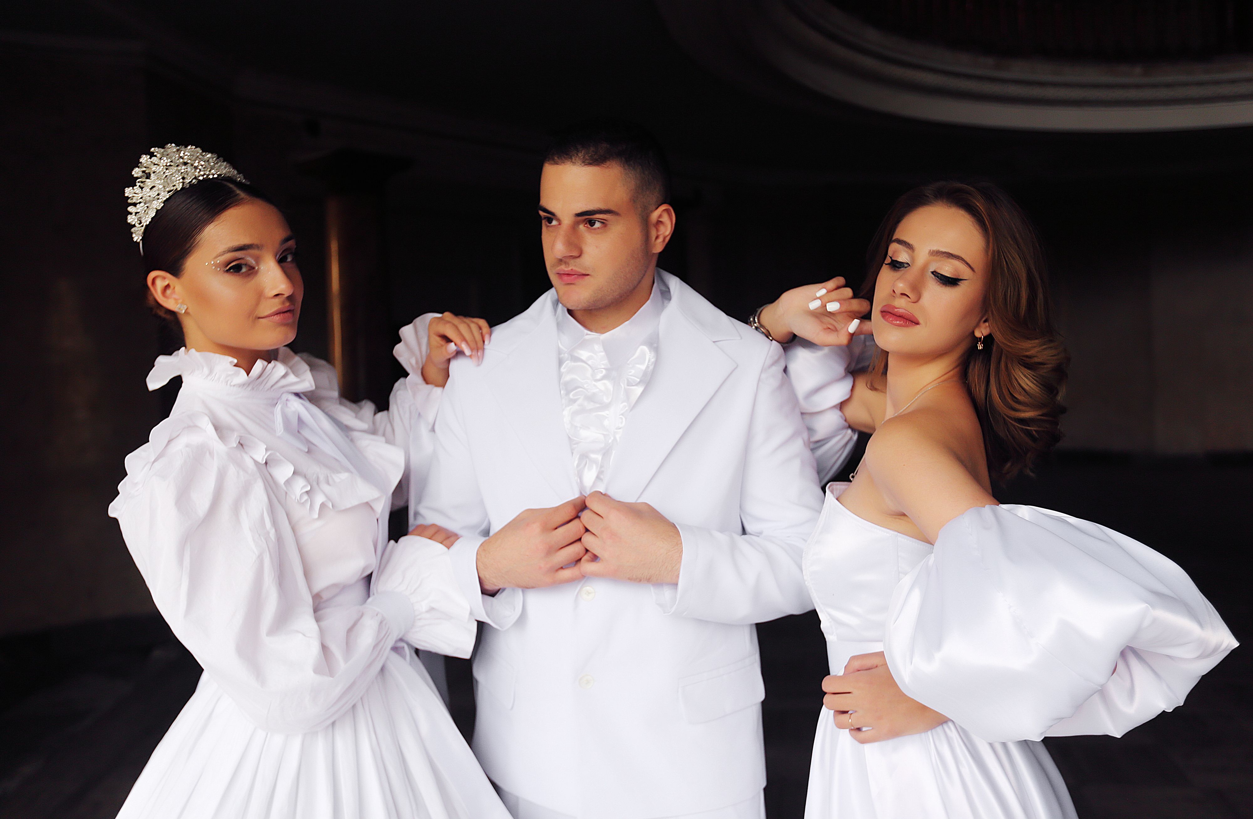 A stylish trio dressed in white formal outfits posing indoors with elegance and grace.
