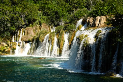 Free Stunning view of cascading waterfalls surrounded by lush greenery on a sunny day. Stock Photo