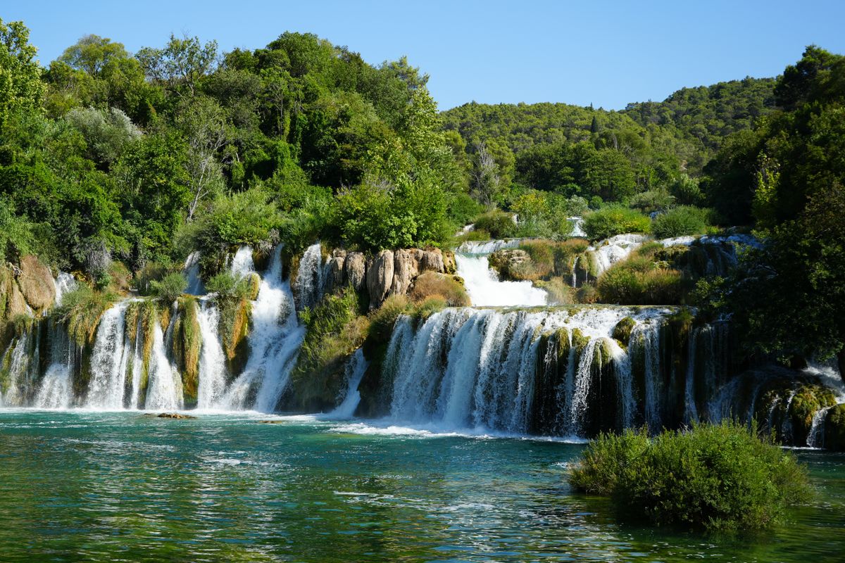 Cascading waterfalls flowing over travertine barriers surrounded by lush green forest at Krka National Park, Croatia