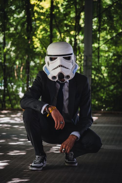 Free A person in a stormtrooper helmet and suit crouches in an outdoor setting, blending cosplay with style. Stock Photo