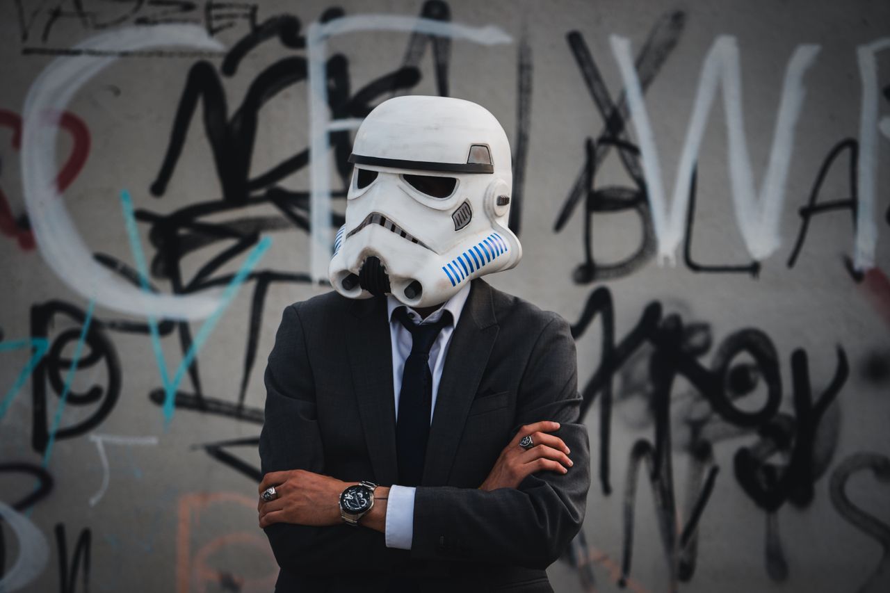 man in suit and stormtrooper helmet standing against a graffiti wall b