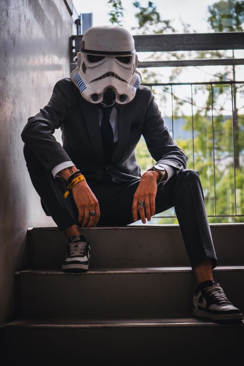 Free Business attire meets sci-fi cosplay as a man poses on outdoor stairs in a stormtrooper helmet. Stock Photo