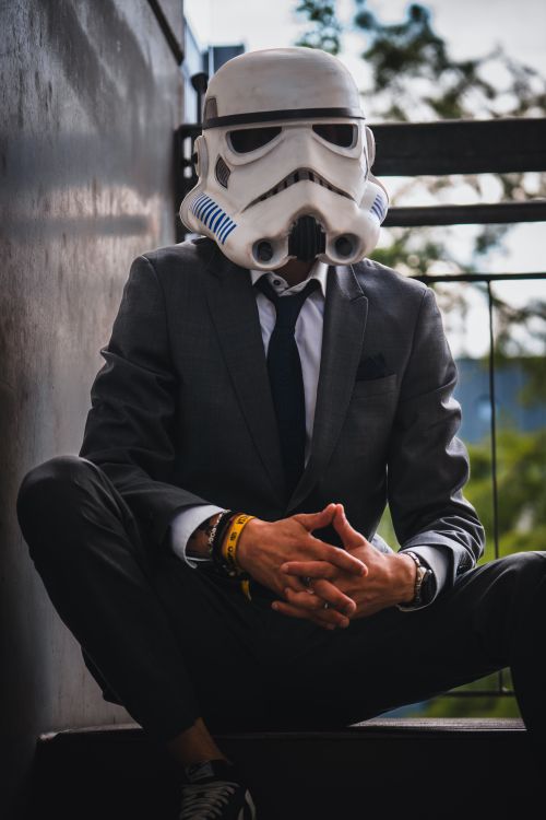 Free A man in a suit with a Stormtrooper helmet sits outdoors, blending classic style with sci-fi flair. Stock Photo