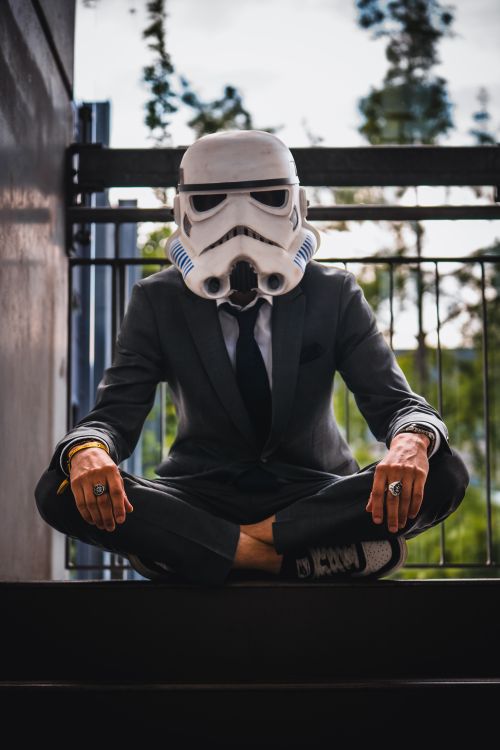 Free A person wearing a stormtrooper helmet and suit meditates outdoors, blending sci-fi with fashion. Stock Photo