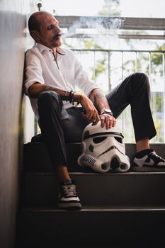 Stylish male model in casual attire relaxing outdoors with a Stormtrooper helmet, exuding a cool and retro vibe.