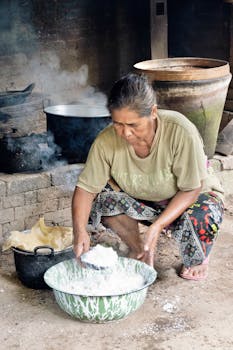An elderly woman prepares food in a rustic kitchen setting, showcasing traditional cooking methods.