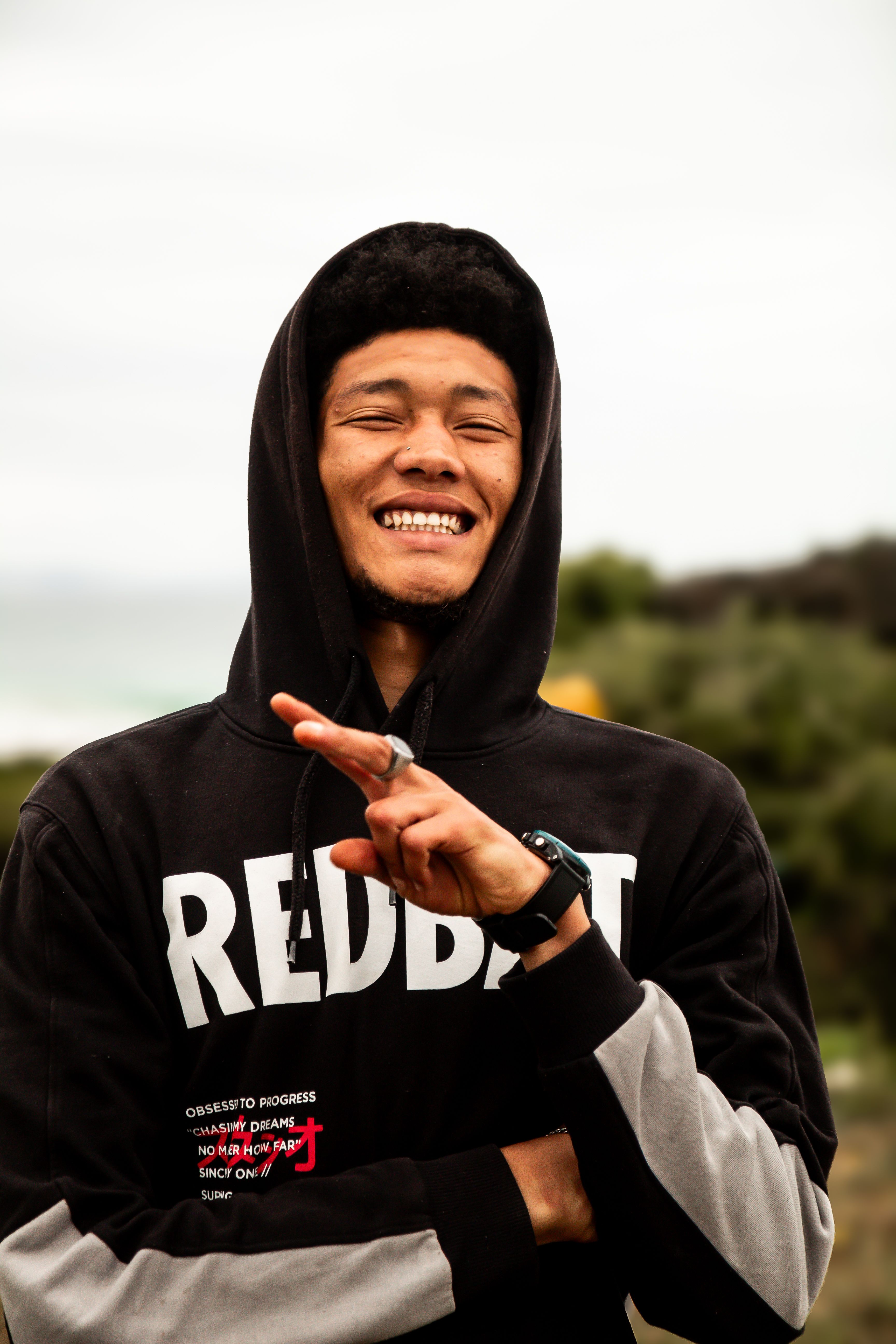 A cheerful man wearing a hoodie poses outdoors with a peace sign, exuding warmth.
