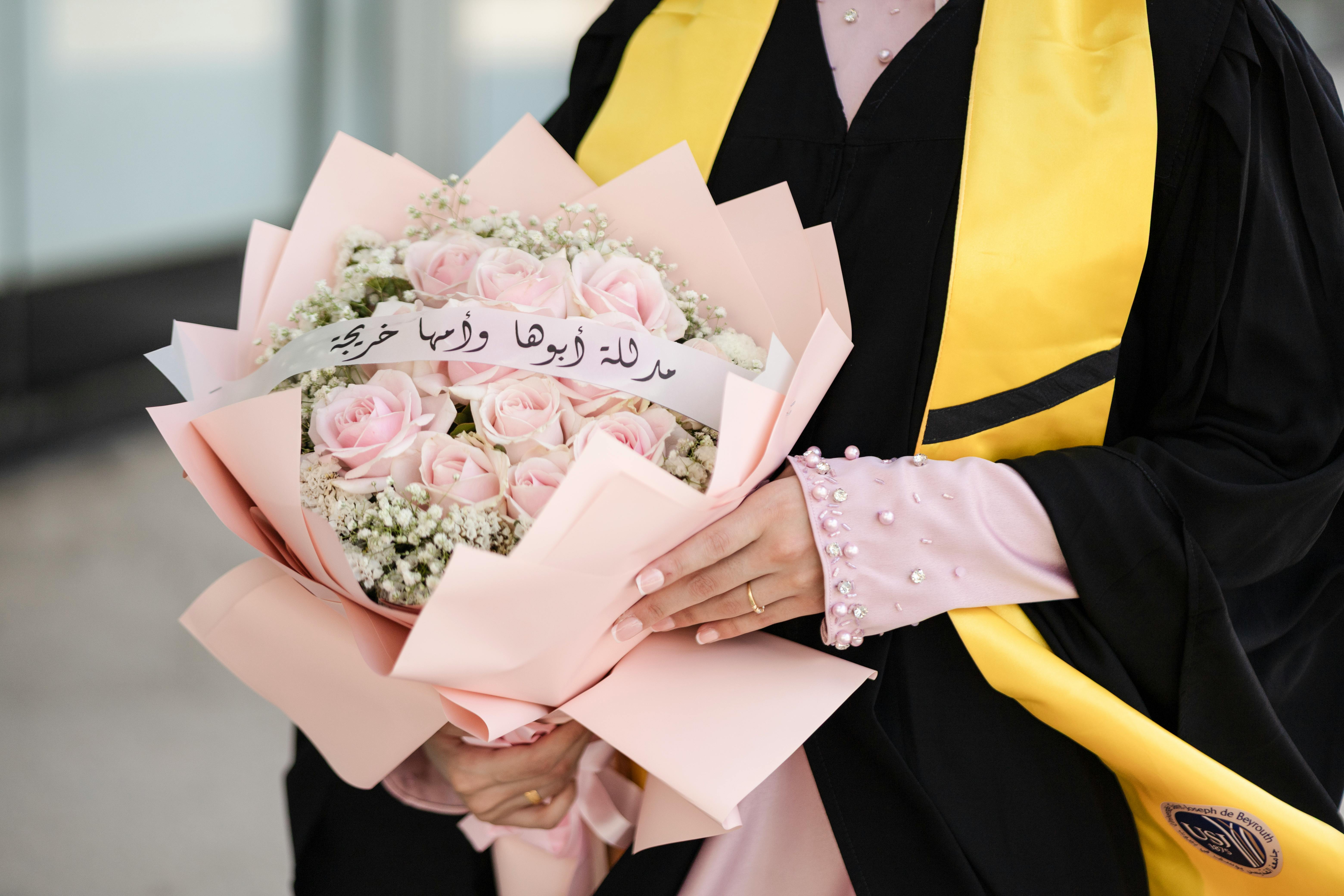 Graduation celebration with bouquet of pink roses, gown, and handwritten message.