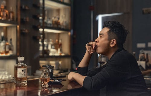 Asian man resting in bar with cigar and whiskey