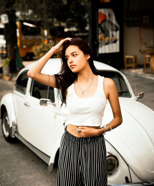 Free A young woman poses stylishly by a classic white car in a city setting, conveying a modern yet vintage vibe. Stock Photo