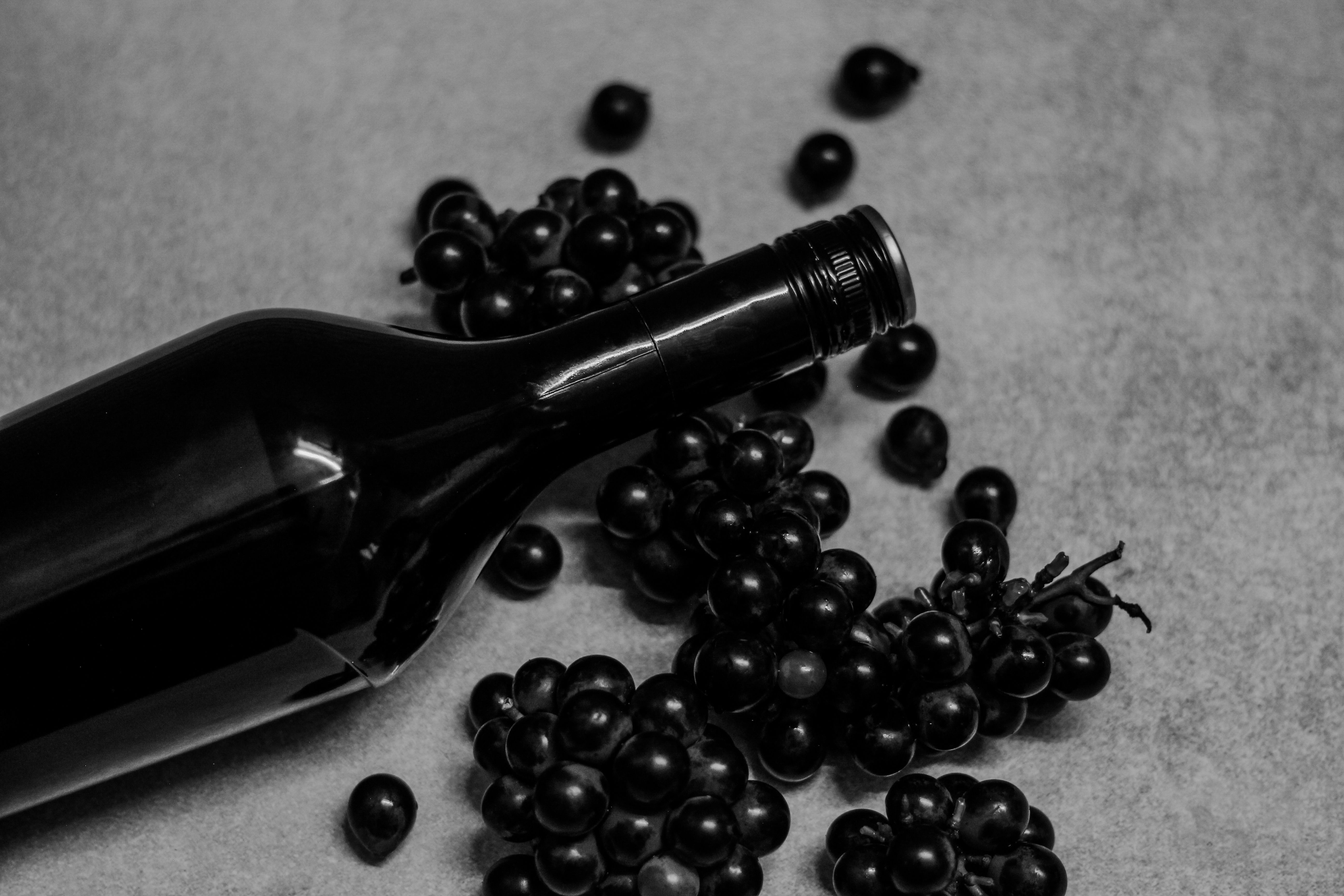 Black wine bottle with grapes arranged artistically. Perfect for still life photography enthusiasts. (Photo by shafi mahammad on Pexels)
