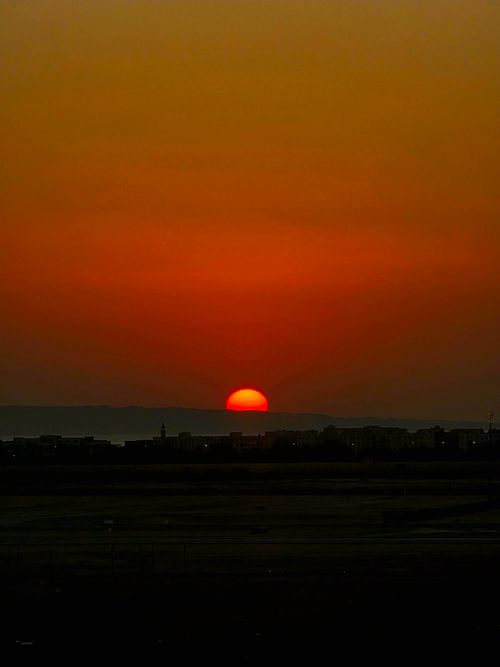 Free Captivating view of the sun setting over a silhouetted cityscape with vivid red and orange hues. Stock Photo