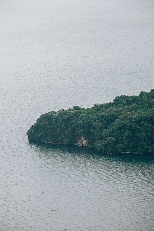 Free Aerial view of a lush green island with rocky cliffs surrounded by calm sea water. Stock Photo