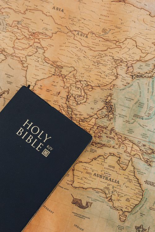 Free A black Holy Bible placed on a vintage map highlighting Asia and Australia for a religious and travel concept. Stock Photo