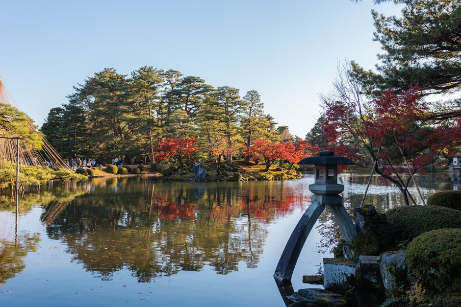 Beautiful autumn landscape at Kenrokuen Garden with vibrant foliage reflected on a tranquil pond.
