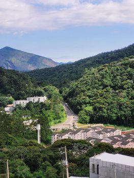 Lush green mountains surround a residential area under a bright blue sky.