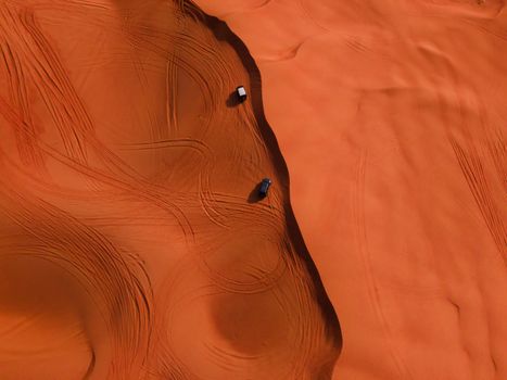 Stunning aerial shot of two cars making tracks on vibrant red sand dunes in a desert landscape.
