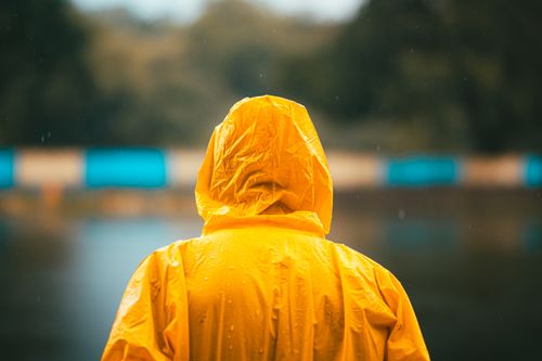 Free Person in a vibrant yellow raincoat standing by a calm lake on a rainy day. Stock Photo