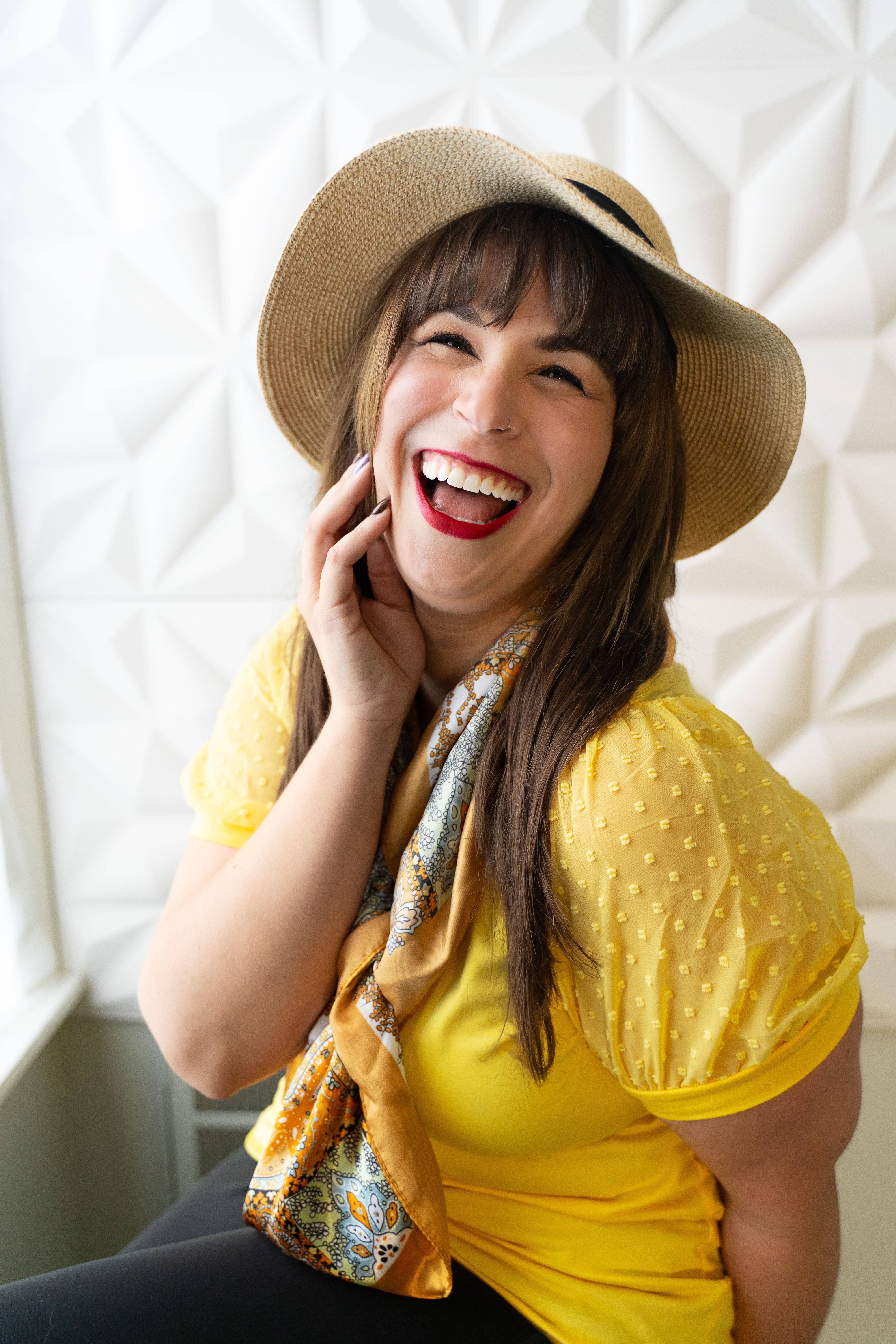 A cheerful woman in a yellow top and hat enjoying a lighthearted moment indoors.