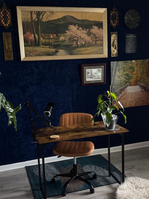 Free Elegant home workspace featuring a desk, plants, and framed art on navy walls. Stock Photo