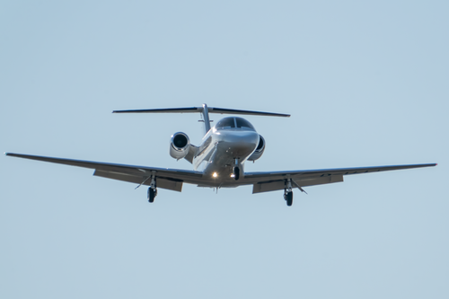 Free A sleek silver private jet approaches landing under a clear blue sky. Stock Photo