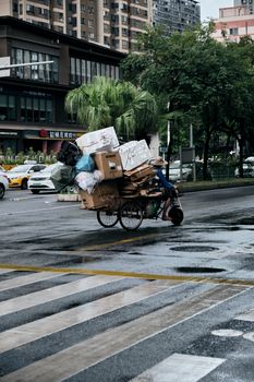 A man on a tricycle cart loaded with boxes on a rainy city street.