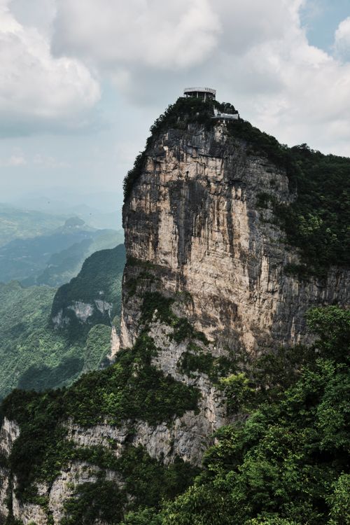 Free Impressive mountain peak with a structure atop, surrounded by lush greenery and dramatic skies. Stock Photo